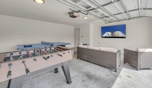 Une pièce comprenant une table de baby-foot, deux canapés en osier et une œuvre d’art accrochée au mur.