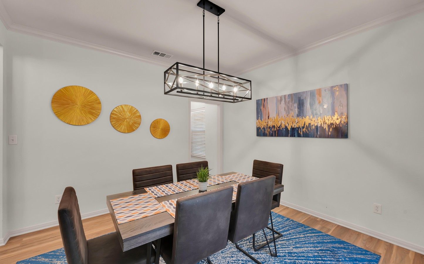 A dining area with a rectangular table, six chairs, a chandelier, and wall art.