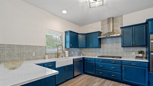 Una cocina moderna con armarios azules, encimera blanca y campana extractora de acero inoxidable.