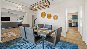 Un comedor con una mesa rectangular, seis sillas y un lámpara colgante. Se ve una cocina a través de un vano abierto.