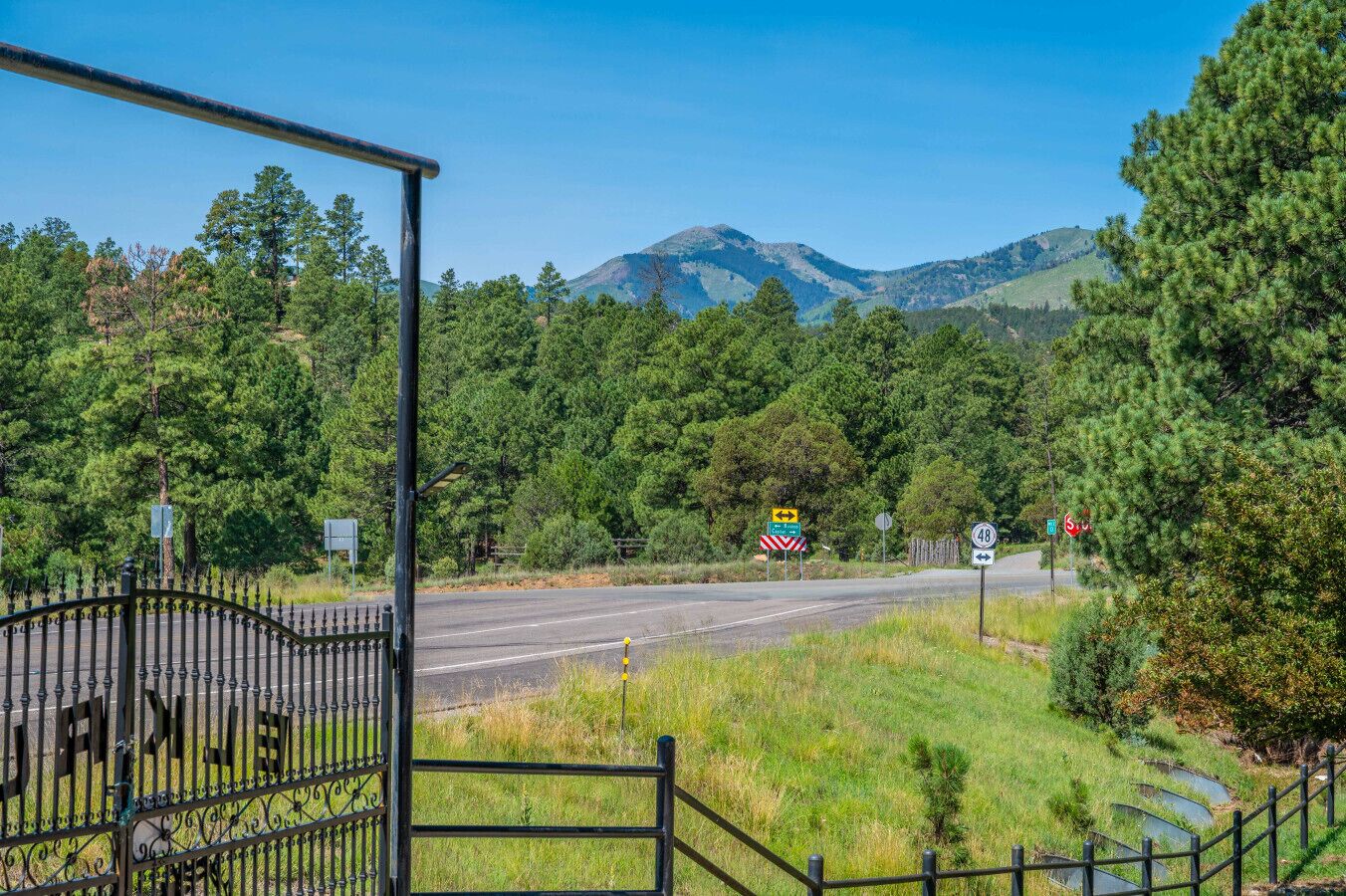 A rural road with a metal gate, road signs, and a mountainous backdrop.