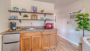 A compact kitchen with wooden cabinets, a built-in dishwasher, and a granite countertop. There are multiple shelves above the counter holding various kitchen items and a microwave. - Pet Friendly | Dog Run | New Remodel | Wildlife (Alto)