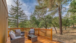 Eine Holzterrasse mit Korbmöbeln und Geländer, umgeben von Bäumen.