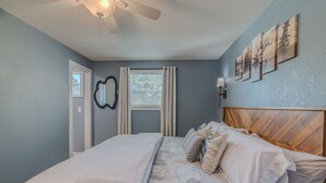 Ein Schlafzimmer mit Bett, Deckenventilator, Fenster mit Vorhängen und Wandbildern.