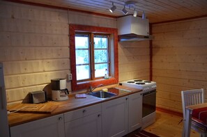 Eine kompakte Küche mit Holzausziehtisch, einem Gasherd, einem Spülbecken und einem Fenster mit Blick auf Bäume.