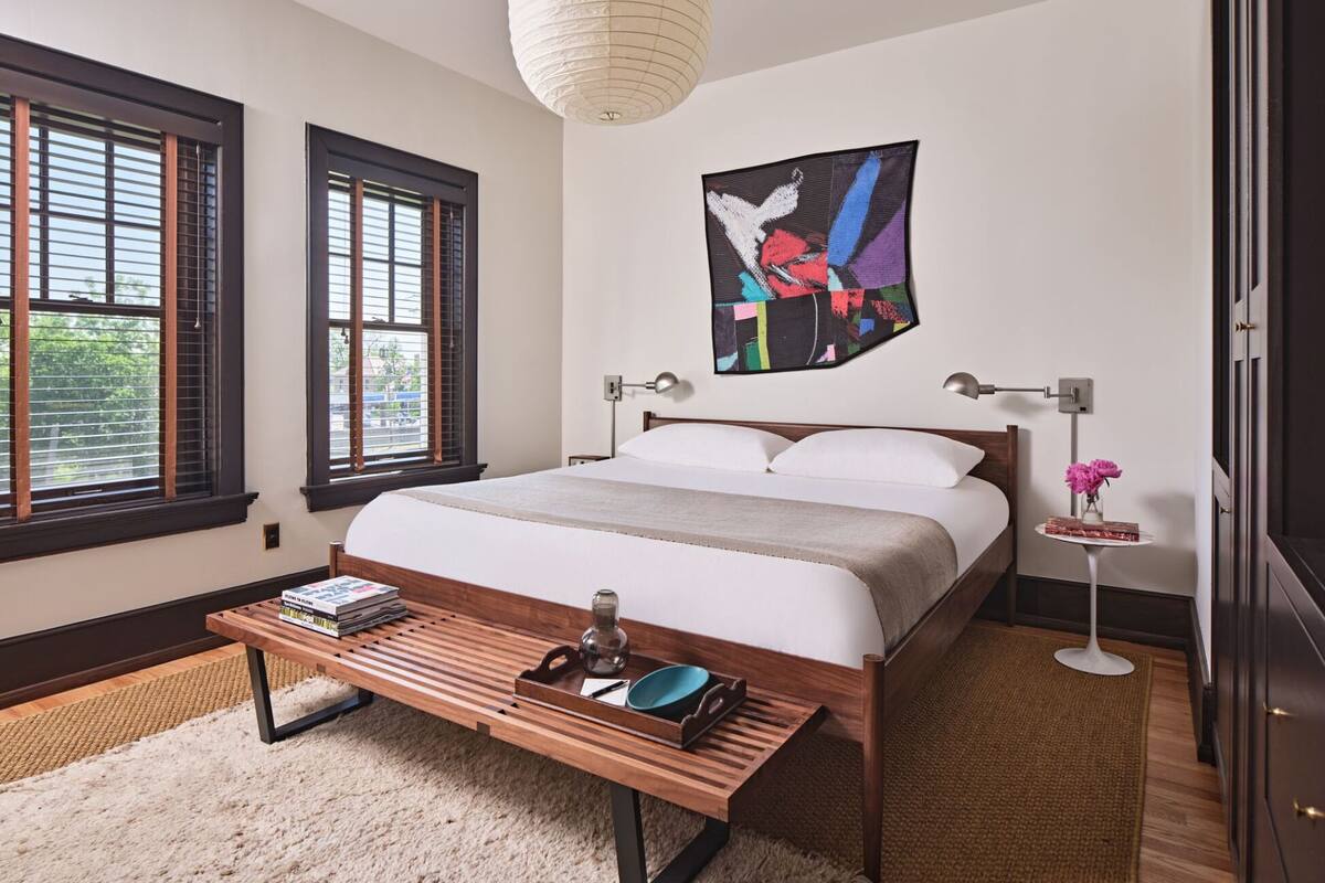 Um quarto moderno com uma cama grande, duas mesas de cabeceira, um banco de madeira e uma obra de arte na parede.