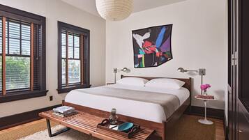 A modern bedroom with a large bed, two bedside tables, a wooden bench, and a wall-mounted artwork.