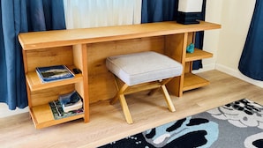 Ein Holztisch mit Regalen, ein gepolsterter Hocker und eine Lampe.