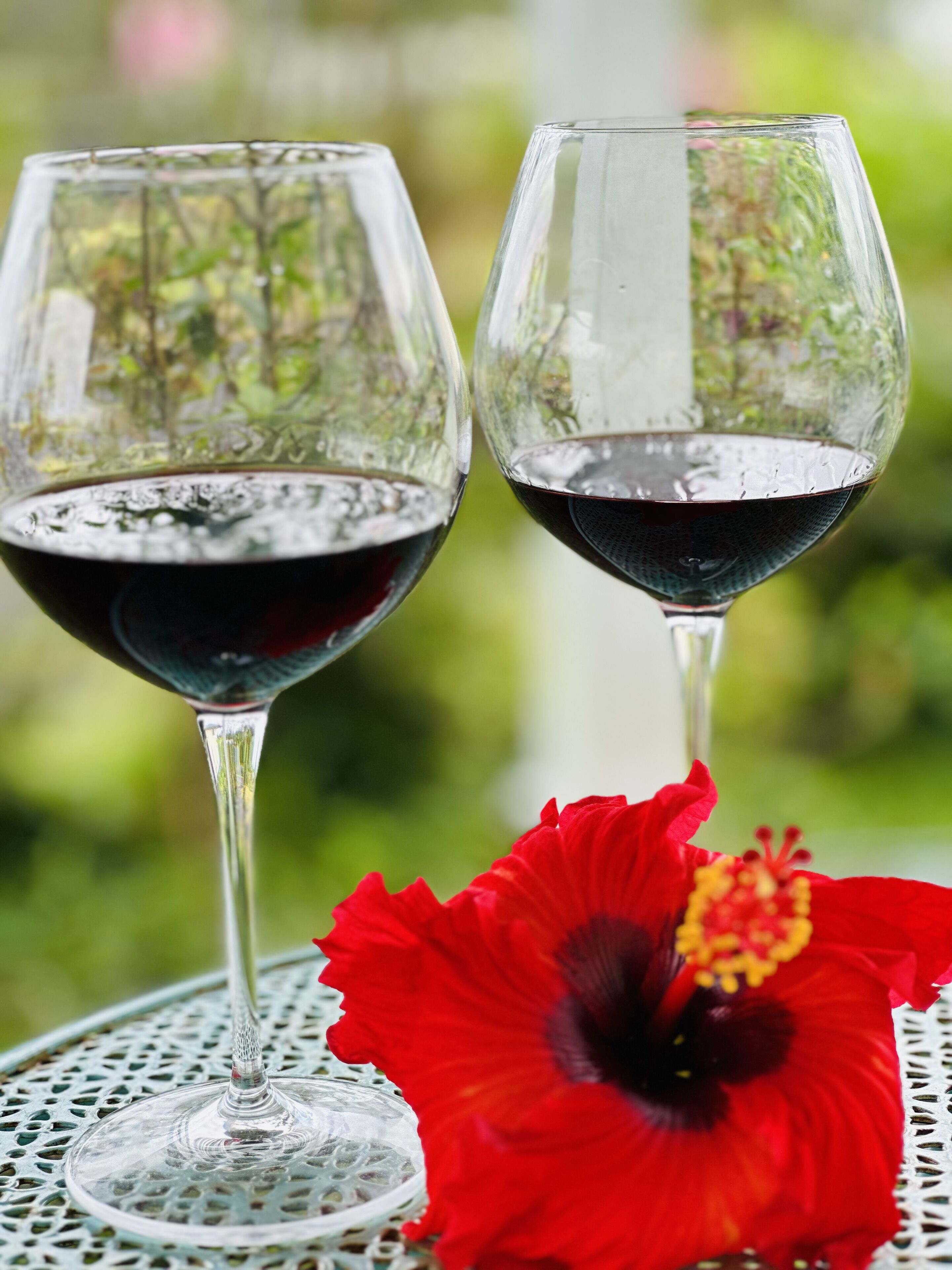 Dos copas de vino sobre una mesa con una flor roja.