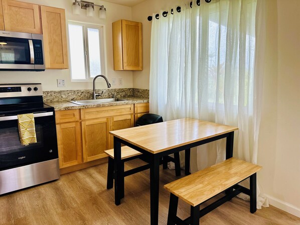 A compact kitchen with wooden cabinets, a stainless steel microwave, a double oven, and a wooden dining table with benches.