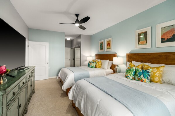 Habitación de hotel con dos camas, ventilador de techo, cómoda y obras de arte en las paredes.