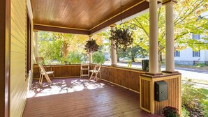 A covered porch with wooden flooring, two wooden chairs, a hanging planter, and a utility box. - Pool Table & More Spacious Family Fun (Canton)