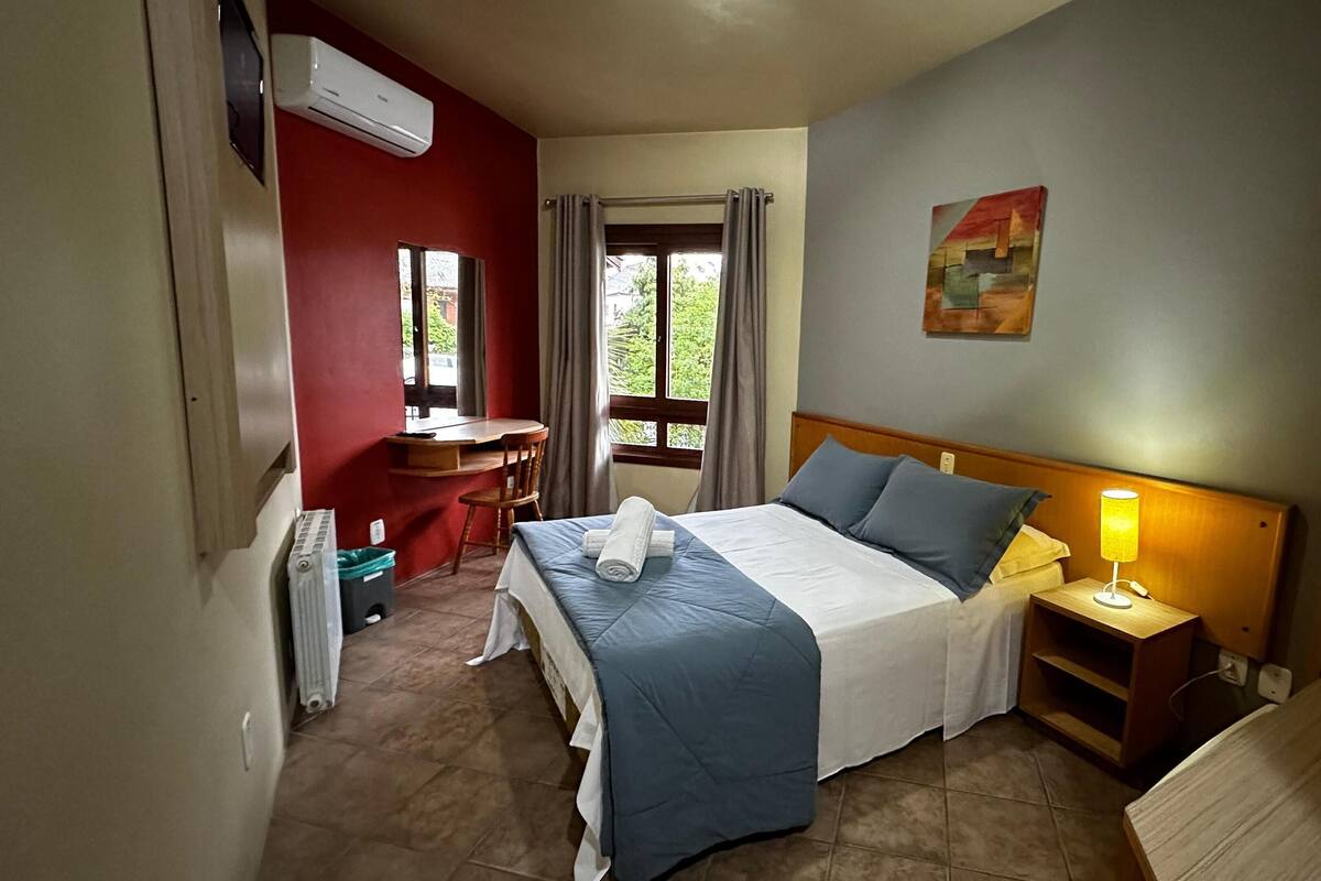 Une chambre d’hôtel comprenant un lit, une table de chevet, une lampe, un bureau, une chaise et une fenêtre avec des rideaux.