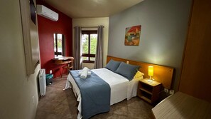 Habitación de hotel con cama, mesita de noche, lámpara, escritorio, silla y ventana con cortinas.