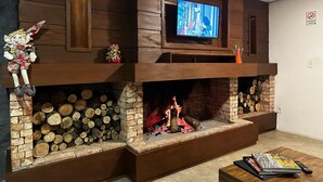 A living room with a fireplace, a television mounted above it, and a plush toy on the mantel. - Pousada Canela Garden (Canela)