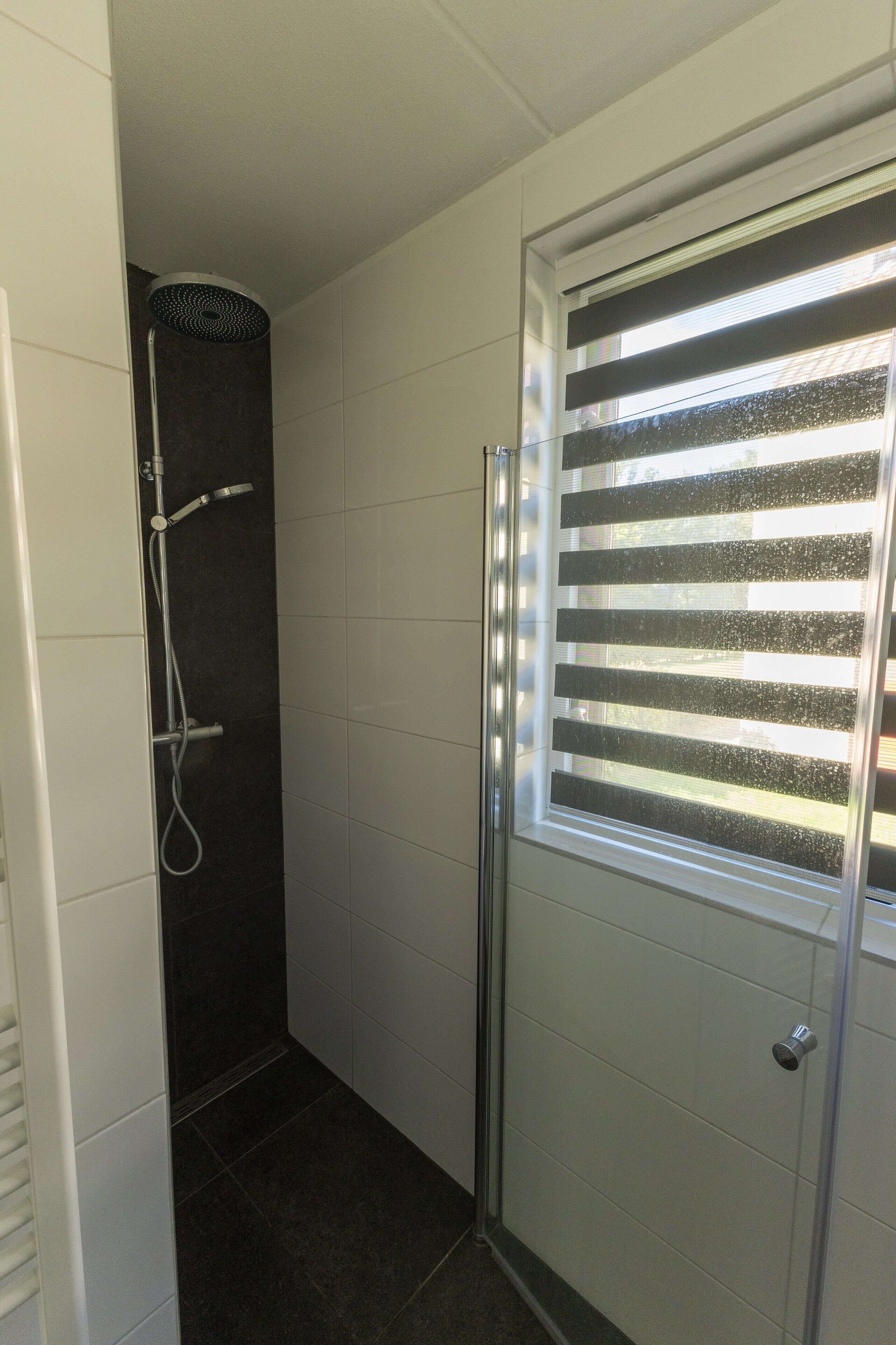 Un baño con ducha, inodoro y ventana con persianas.
