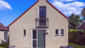 Une maison à deux étages avec un toit rouge, un balcon doté de rampes en métal et une porte verte.
