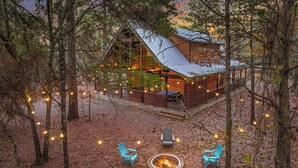 A cabin with a deck, surrounded by trees and a fire pit with chairs. - Beautiful cabin tucked away on almost 1.5 acres (Broken Bow)