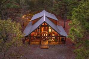 A cabin with a triangular roof, wooden exterior, and a porch with seating. - Beautiful cabin tucked away on almost 1.5 acres (Broken Bow)