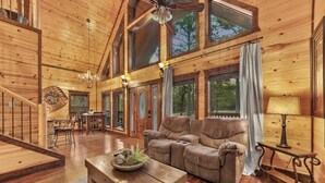 A spacious wooden interior with a large sofa, a wooden coffee table, and a dining area. - Beautiful cabin tucked away on almost 1.5 acres (Broken Bow)