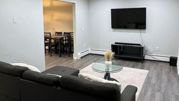 Ein modernes Wohnzimmer mit einem dunkelgrauen Sofa, einem Glastisch und einem flachbildfernseher an der Wand.