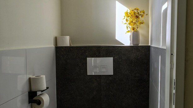 A small, modern bathroom with a toilet, a hand dryer, and a paper towel dispenser. - Holiday Home in Ewijk in a Beautiful Area (Ewijk)
