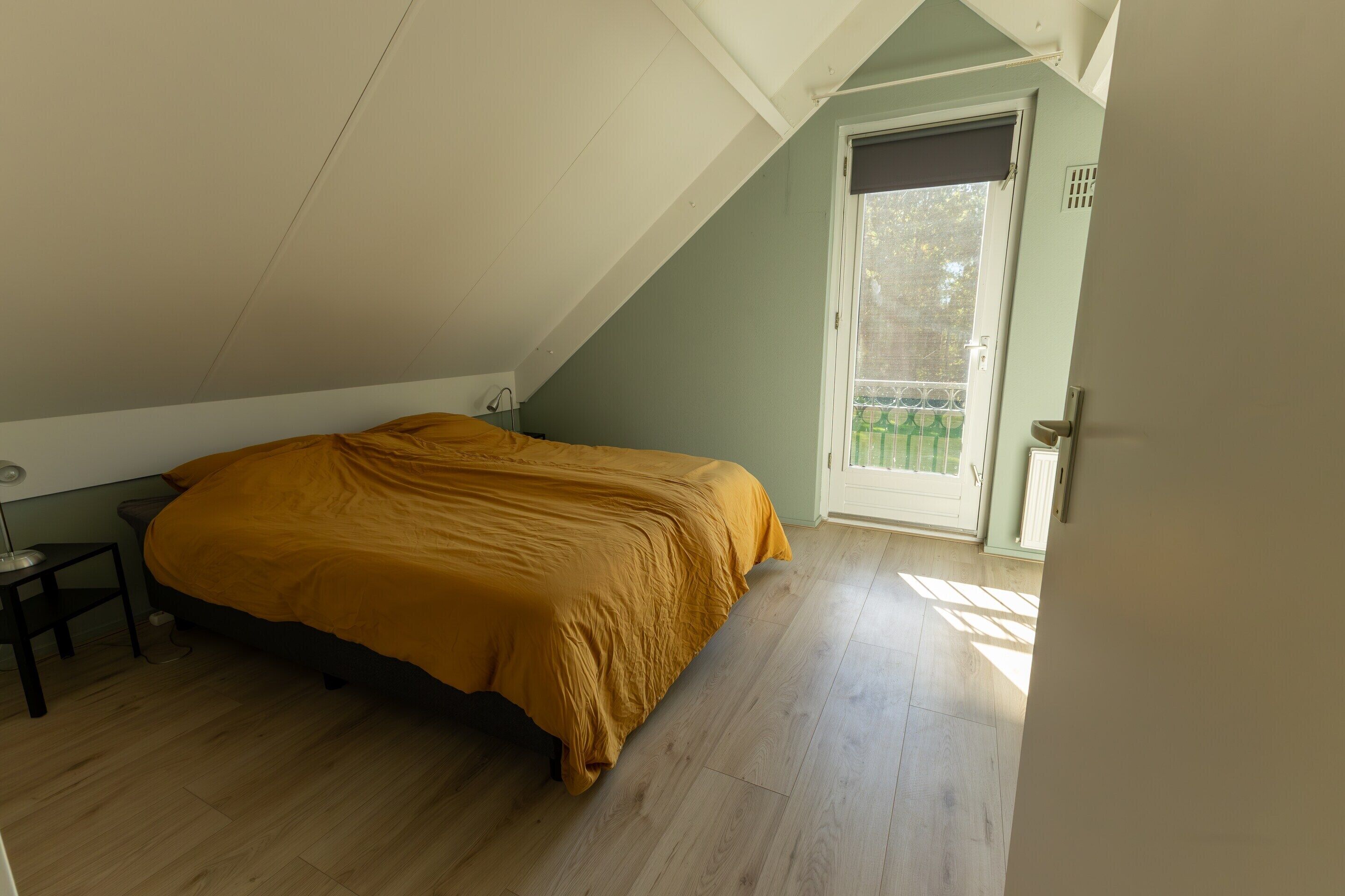 A bedroom with a bed, a nightstand, and a door to a balcony.