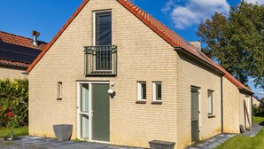 A two-story brick house with a green door, a small balcony, and a chimney. - Holiday Home in Ewijk in a Beautiful Area (Ewijk)