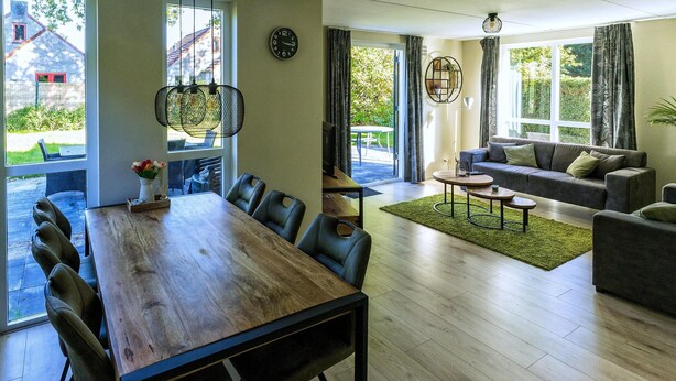 A spacious living area with a wooden dining table, a sofa, and a coffee table. There are large windows providing natural light and views of the outdoors. - Holiday Home in Ewijk in a Beautiful Area (Ewijk)