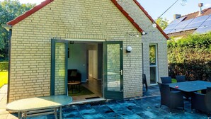 A small brick house with a sloped roof, a sliding glass door entrance, and a patio area with a table and chairs. - Holiday Home in Ewijk in a Beautiful Area (Ewijk)