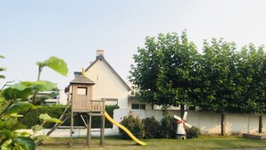 En trælegeplads med rutsjebane og et lille huslignende hus i en græsplæne.