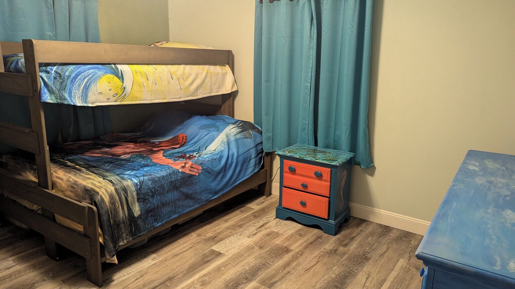 A bunk bed with a colorful bedspread, a small nightstand with drawers, and a blue dresser.