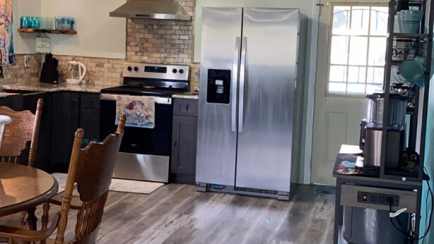 A kitchen with a stainless steel refrigerator, a stove, and a water dispenser. There is a dining table with chairs and a window with blinds.