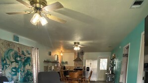 A living room with a sofa, a coffee table, and a dining area with chairs and a table. There is a kitchen area with a refrigerator and a stove.
