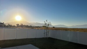 A backyard with a white fence, a small tree, and a clear view of distant mountains and a body of water during sunset. -  Beautiful home near Thanksgiving Point. Views of Utah Lake, sunrise and sunset (American Fork)