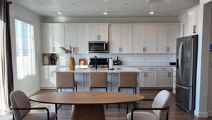 A modern kitchen with white cabinets, a central island with seating, a stainless steel refrigerator, and a microwave. -  Beautiful home near Thanksgiving Point. Views of Utah Lake, sunrise and sunset (American Fork)