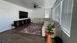 A living room with a sectional sofa, a flat-screen TV, a ceiling fan, and a wooden coffee table with decorative items. -  Beautiful home near Thanksgiving Point. Views of Utah Lake, sunrise and sunset (American Fork)