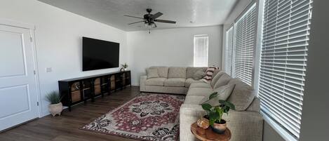 A living room with a sectional sofa, a flat-screen TV, a ceiling fan, and a wooden coffee table with decorative items.