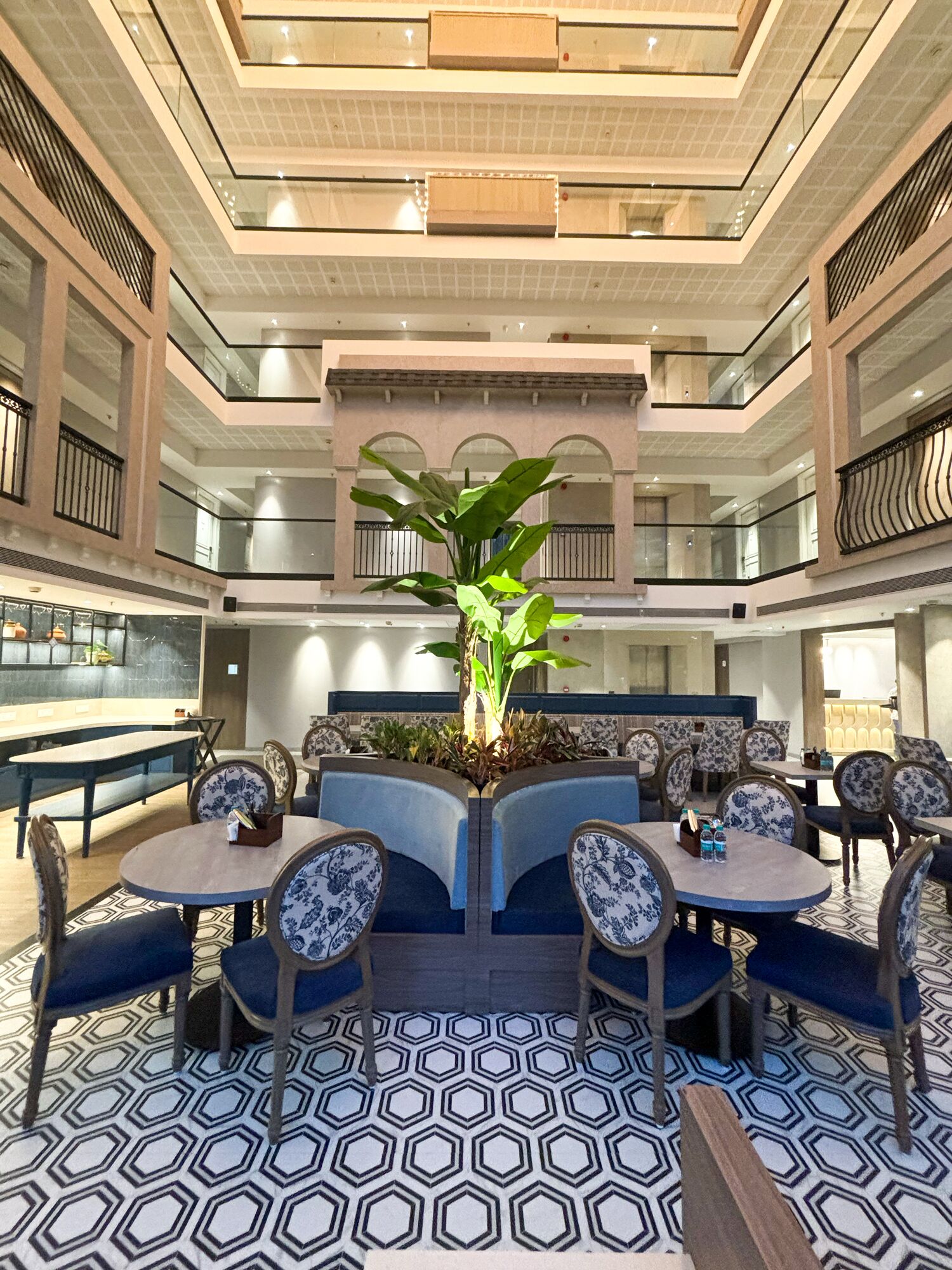 A multi-level lobby with a central seating area, a large plant, and a patterned floor.
