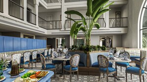 A spacious indoor dining area with multiple seating arrangements, including booths and round tables. There are potted plants and a large central plant adding greenery. The flooring features a geometric pattern, and the walls are adorned with decorative moldings. - Meritas Auberge Calangute Goa (Calangute)
