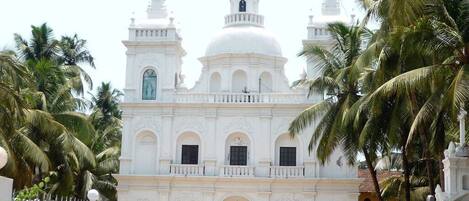 A white colonial-style church with a central dome and two bell towers, surrounded by palm trees.