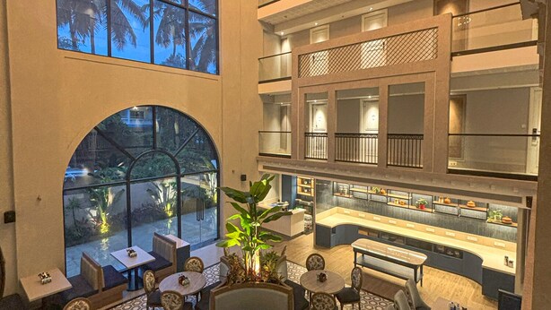 A multi-level hotel lobby with seating areas, a central bar, and a view of palm trees outside. - Meritas Auberge Calangute Goa (Calangute)