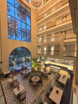A multi-level hotel lobby with seating areas, a central bar, and a view of palm trees outside. - Meritas Auberge Calangute Goa (Calangute)