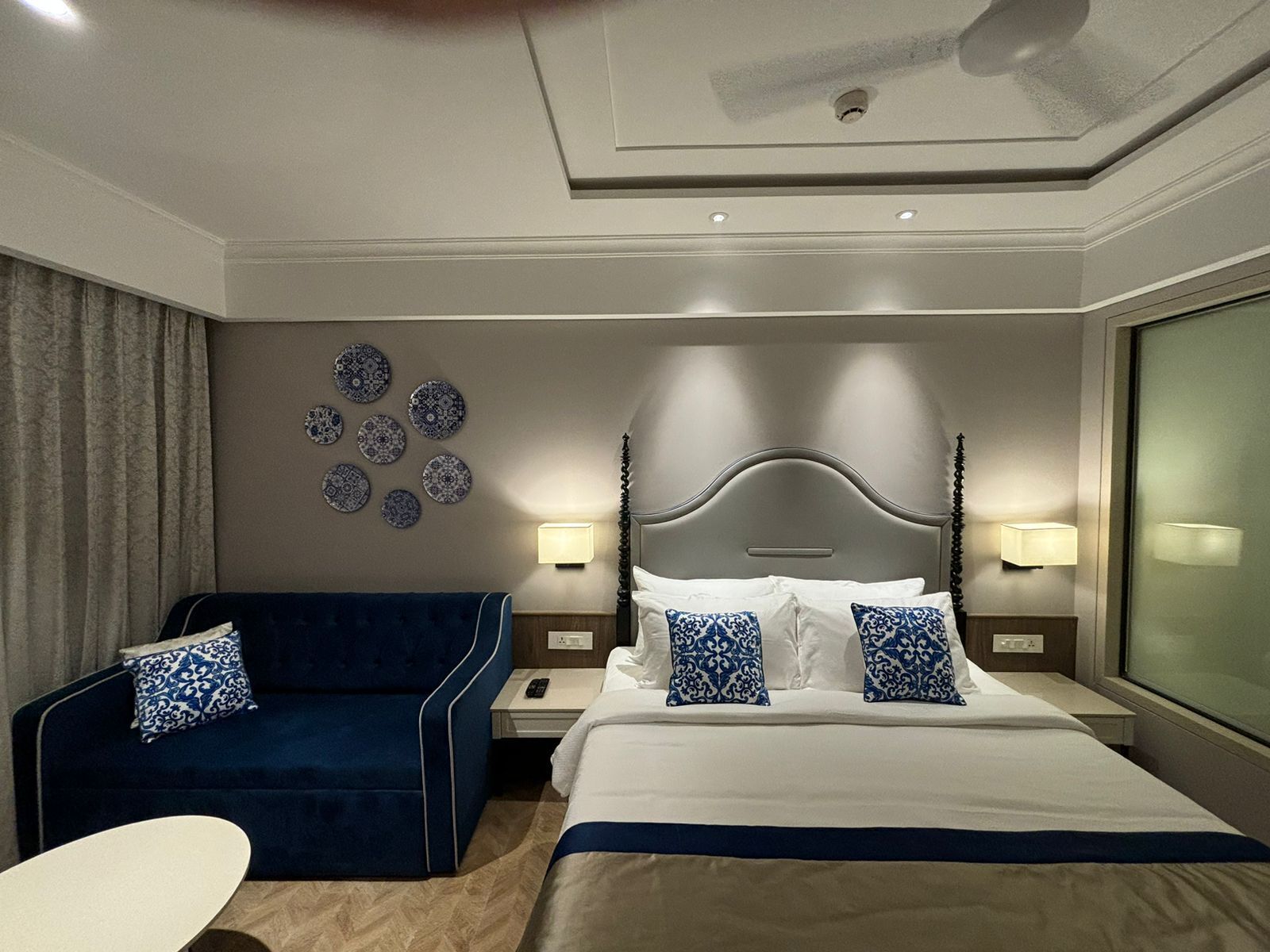 Una habitación de hotel con una cama, un sofá azul, una mesita de noche con una lámpara y una pared decorada con platos.