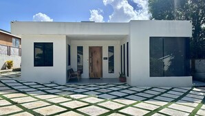 Ein modernes Haus mit weißer Fassade, einer Holztür und einer kleinen Veranda mit einem Stuhl und einem Blumentopf.