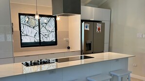 Eine moderne Küche mit einer zentralen Kochinsel, weißen Barhocker und Pendelleuchten.