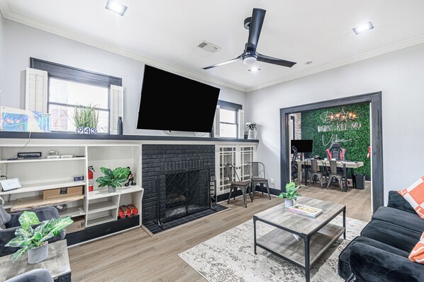A modern living room with a fireplace, a flat-screen TV mounted above it, and a dining area with a green wall and a table. - 3-bedroom house in delightful Houston with WiFi, fitness room, AC (Houston)
