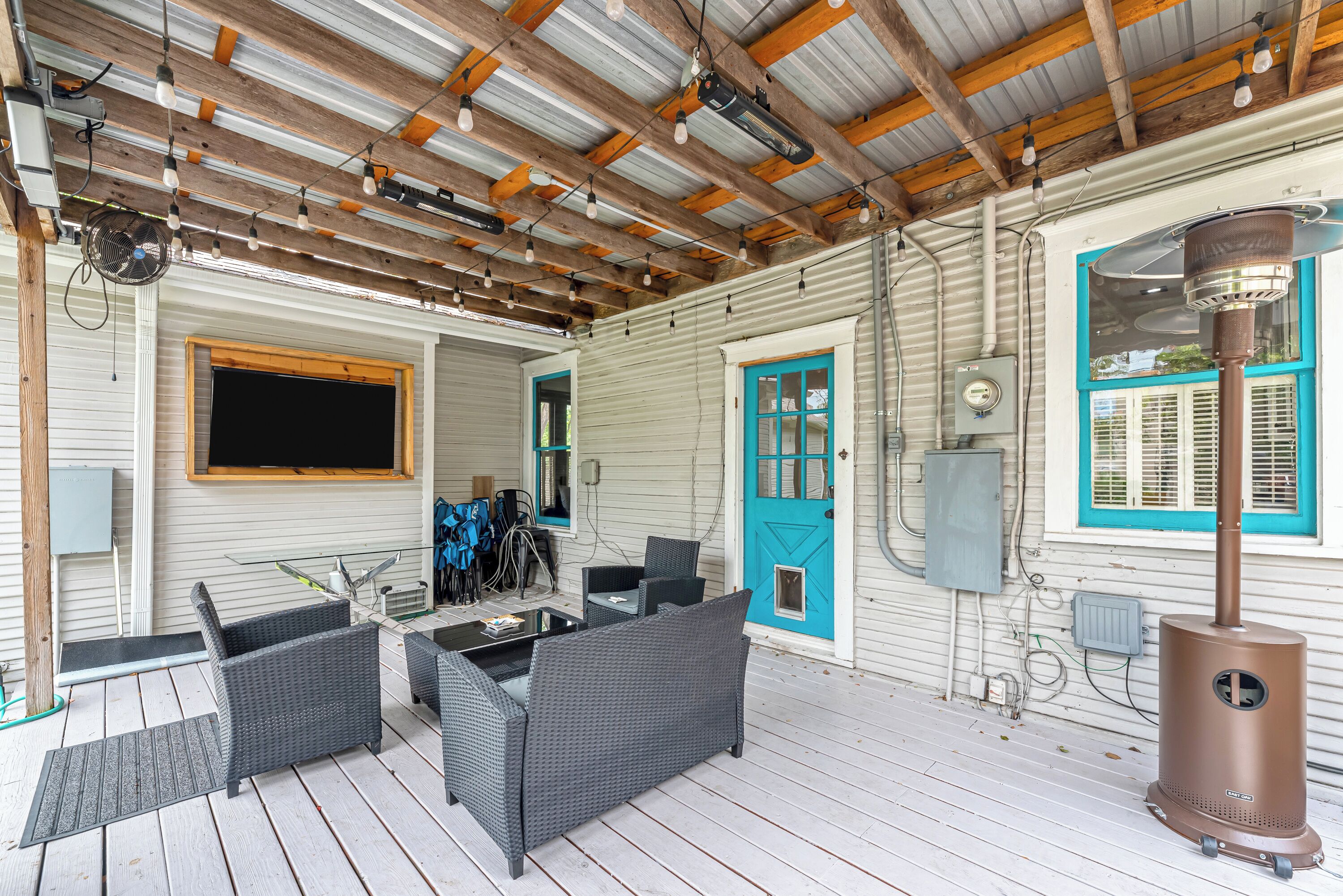 A covered outdoor area with wicker furniture, a wood-framed ceiling, and a wood-burning stove.