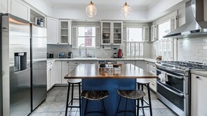 A modern kitchen with white cabinets, stainless steel appliances, a central island with stools, and pendant lighting. - 3-bedroom house in delightful Houston with WiFi, fitness room, AC (Houston)