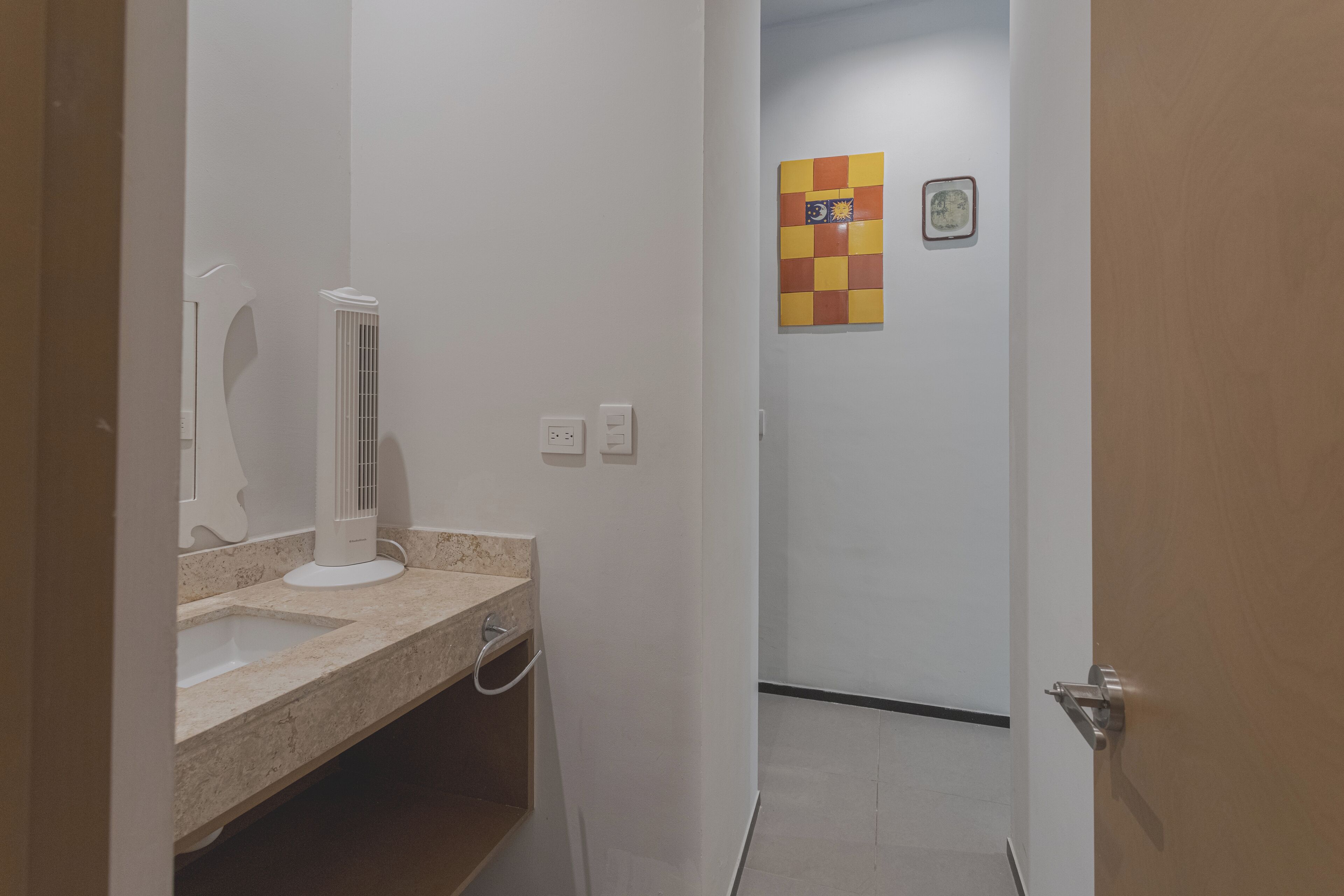 A bathroom with a white vanity, a mirror, and a white pedestal fan.